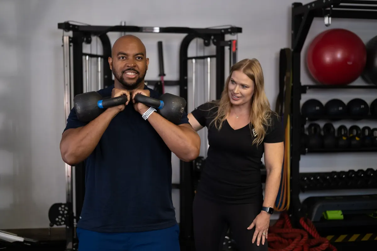 A Formula Fitness coach watching a client hold two kettlebells